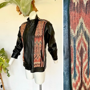 May include: A black leather jacket with a colorful patterned fabric panel on the front and back. The fabric is a traditional ikat design in shades of red, orange, blue, and white.