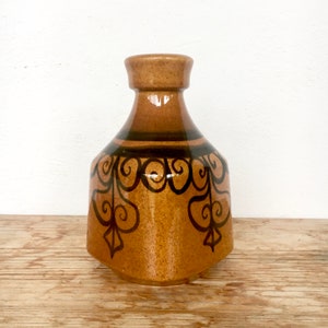 May include: A brown ceramic vase with a geometric design in black. The vase has a wide base and a narrow neck.