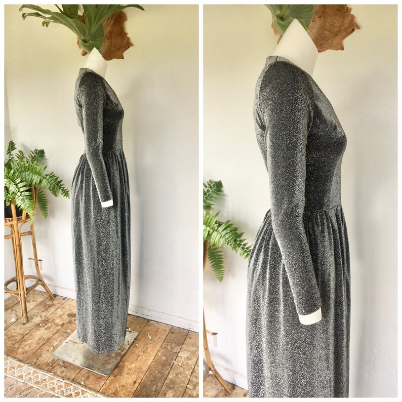 May include: A long-sleeved silver and black glitter dress with a V-neckline. The dress has a gathered waist and a flowing skirt.