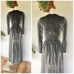 May include: A long, silver, sparkly dress with a V-neck and long sleeves. The dress has a fitted bodice and a flowing skirt.