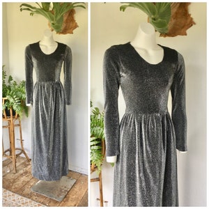 May include: A long-sleeved silver and black sparkly dress with a round neckline. The dress has a fitted bodice and a flowing skirt.