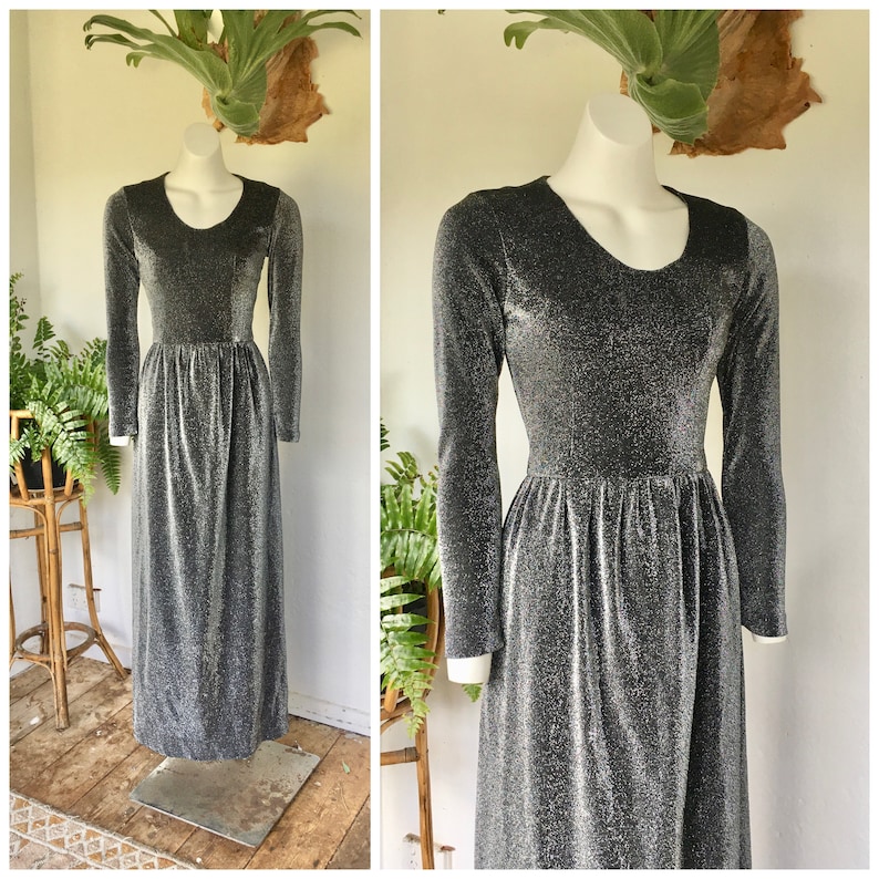 May include: A long-sleeved silver and black sparkly dress with a round neckline. The dress has a fitted bodice and a flowing skirt.