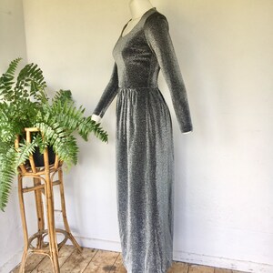 May include: A silver long-sleeved maxi dress with a sparkly texture. The dress has a scoop neckline and a fitted bodice. The skirt is flowing and has a slight A-line shape.