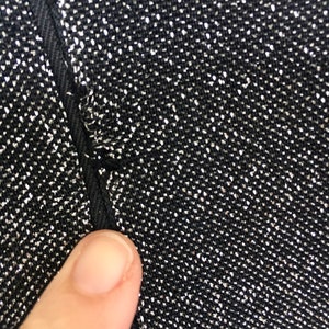 May include: Close-up of a black fabric with silver glitter woven into the fabric. The fabric has a seam running down the side.