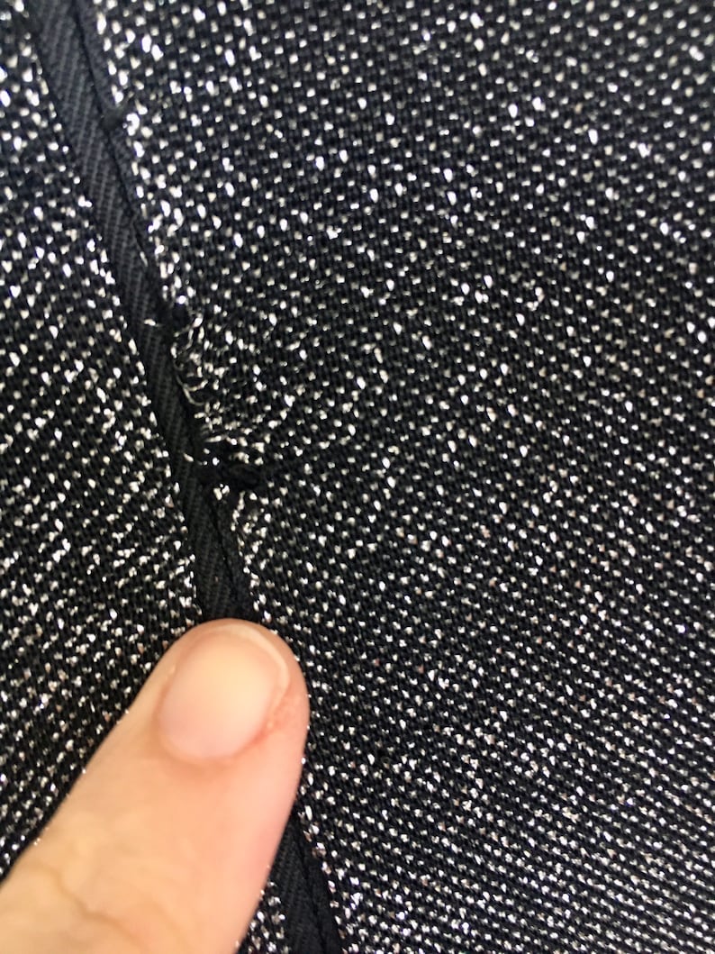May include: Close-up of a black fabric with silver glitter woven into the fabric. The fabric has a seam running down the side.