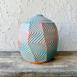 Könnte beinhalten: Eine handgefertigte Keramikvase mit geometrischem Muster. Die Vase hat eine Kombination aus Türkis, Pfirsich und Orange. Die Vase ist etwa 18 cm hoch und 15 cm breit, mit einer strukturierten Oberfläche und einer abgerundeten Form.