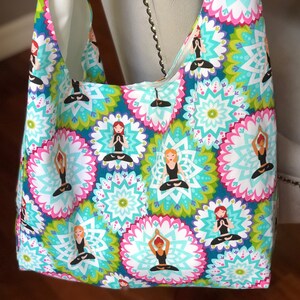 May include: A colorful tote bag with a repeating pattern of mandala-like designs and stylized figures in yoga poses. The figures are all wearing pink, blue, and green clothing.