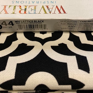 May include: A close-up of black and white fabric with a geometric pattern. The fabric is labeled "WV Lattice Black" and has a care instruction label with details about washing and drying. The fabric is 54 inches (127 cm) wide and 9 yards (822 cm) long.