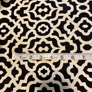 May include: Black and white fabric with a geometric pattern. The pattern is made up of repeating shapes that resemble a trellis or lattice. A measuring tape is placed on the fabric, showing that it is 60 inches wide.