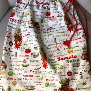 May include: White fabric kitchen bag with red drawstring featuring a colorful print of various ingredients and instructions for making guacamole, salsa, and cowboy chili. The text includes "Kickin' Guacamole", "Tomato Salsa", and "Cowboy Chili".