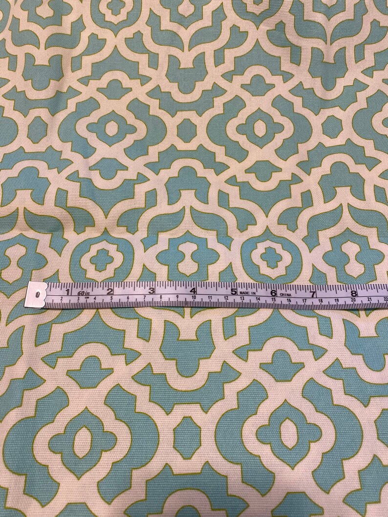 May include: A close-up of a fabric with a repeating geometric pattern. The pattern is made up of light blue and white shapes on a cream background. A ruler is visible at the bottom of the image.