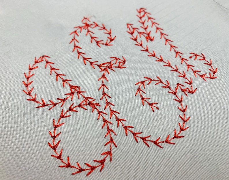May include: A light grey fabric featuring a decorative embroidery pattern stitched in vibrant red thread. The design consists of continuous, flowing lines formed by a repeating feather stitch, creating an organic, vine-like shape across the surface.