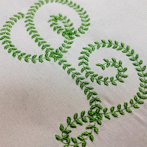May include: Green embroidered design of a double circle on a white fabric background.