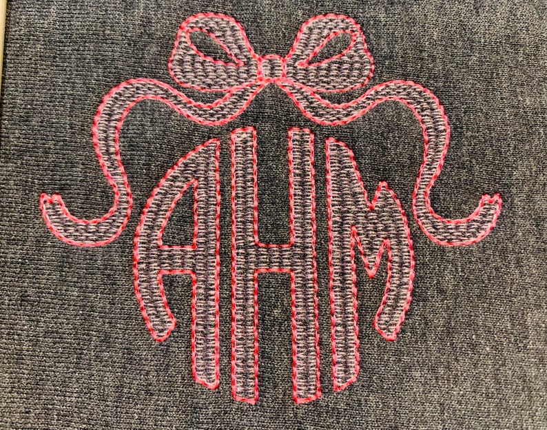 May include: Embroidered monogram with the letters AHM, encircled by a bow. The letters and bow are outlined in bright pink thread, set against a textured gray background. The design is likely for a personalized item.