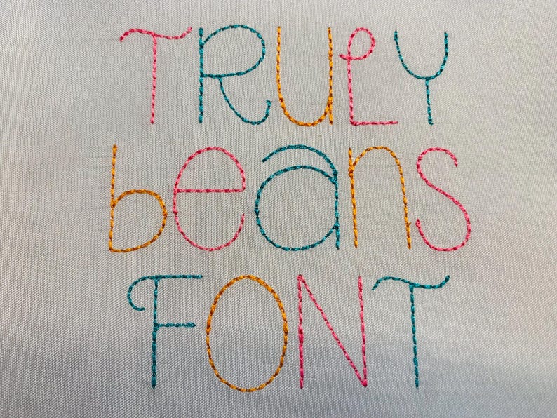 May include: A light gray fabric surface featuring the embroidered text "TRULY beans FONT" in a multi-colored stitch pattern. The letters are stitched in alternating shades of teal, orange, and pink, creating a vibrant and textured appearance.