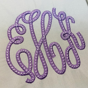 Peut inclure: Une surface en tissu gris clair présentant un monogramme brodé violet avec une police cursive décorative. La broderie se compose de trois lettres entrelacées cousues avec un contour en fil violet et une ligne blanche pointillée au centre.