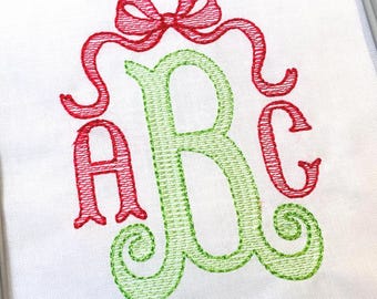 May include: A white fabric surface featuring an embroidered monogram with the letters ABC. The letter B is large and light green, while the letters A and C are smaller and red. A red embroidered bow sits above the letters on the white fabric.
