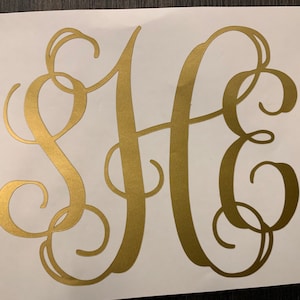 Puede incluir: Pegatina con monograma dorado con las letras S, H y E en una escritura fluida y elegante. Las letras se superponen y se entrelazan, creando un dise&ntilde;o decorativo. La pegatina est&aacute; sobre un fondo blanco.