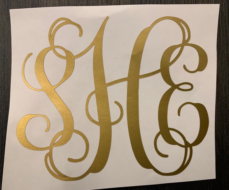 Puede incluir: Pegatina con monograma dorado con las letras S, H y E en una escritura fluida y elegante. Las letras se superponen y se entrelazan, creando un dise&ntilde;o decorativo. La pegatina est&aacute; sobre un fondo blanco.