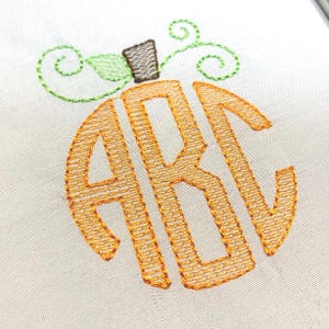 May include: An embroidery design on white fabric featuring the letters ABC in a circular orange pumpkin shape. The pumpkin has a brown stem and green stitched vines and a single green leaf extending from the top of the orange monogram.