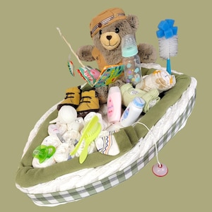 May include: A diaper cake shaped like a boat with a teddy bear wearing a fishing vest and holding a fishing rod. The boat is filled with baby supplies, including diapers, wipes, lotion, and a bottle.