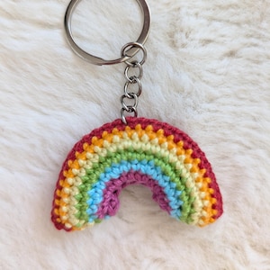 Könnte beinhalten: Ein handgefertigter Regenbogen-Schlüsselanhänger aus Häkelarbeit. Der Regenbogen hat leuchtende Farben wie Rot, Orange, Gelb, Grün, Blau und Lila. Der Schlüsselanhänger hat einen silbernen Metallring und eine Kette.