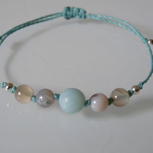 May include: A turquoise string bracelet with five beads, including a light blue, a white, a grey, and two beige beads.