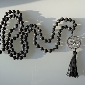 Peut inclure: Mala de perles en pierre de lave noire avec un pendentif en argent en forme de fleur de vie et un pompon noir.