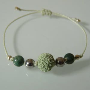 May include: A green and white beaded bracelet with a light green textured bead in the center. The bracelet is made with a white cord and has silver beads on either side of the textured bead.