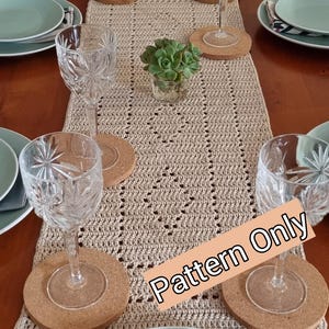 Puede incluir: Un camino de mesa de crochet beige con un patrón geométrico. El camino de mesa está decorado con seis posavasos redondos de corcho y cuatro copas de vino de vidrio transparente. El texto "Pattern Only" está escrito en blanco sobre un rectángulo marrón.