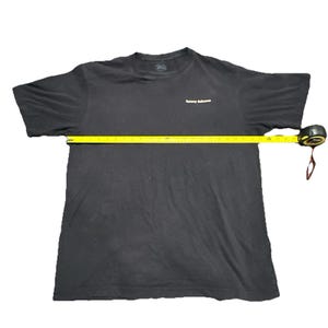 May include: A black t-shirt with the text "Tommy Bahama" in white on the chest. A yellow measuring tape is stretched across the shirt, indicating a measurement of approximately 40 inches.