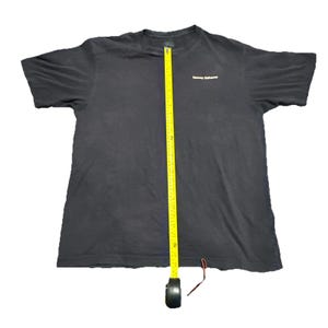 May include: Black t-shirt with the text "Tommy Bahama" in white. A yellow measuring tape is placed vertically on the shirt. The shirt appears to be a size large.
