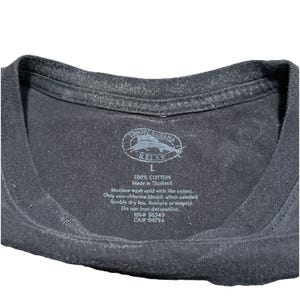 May include: Close-up of a black Tommy Bahama Relax t-shirt tag. The tag includes the brand logo, size 'L', and care instructions. The shirt is made of 100% cotton and made in Thailand.
