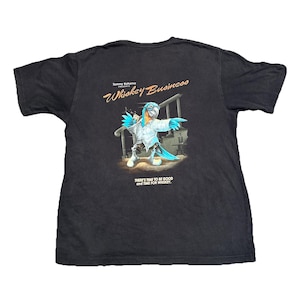 May include: Black t-shirt featuring a colorful parrot illustration with the text "Whiskey Business" and "There's time to be good and time for whiskey." The parrot is wearing a white shirt and pointing.