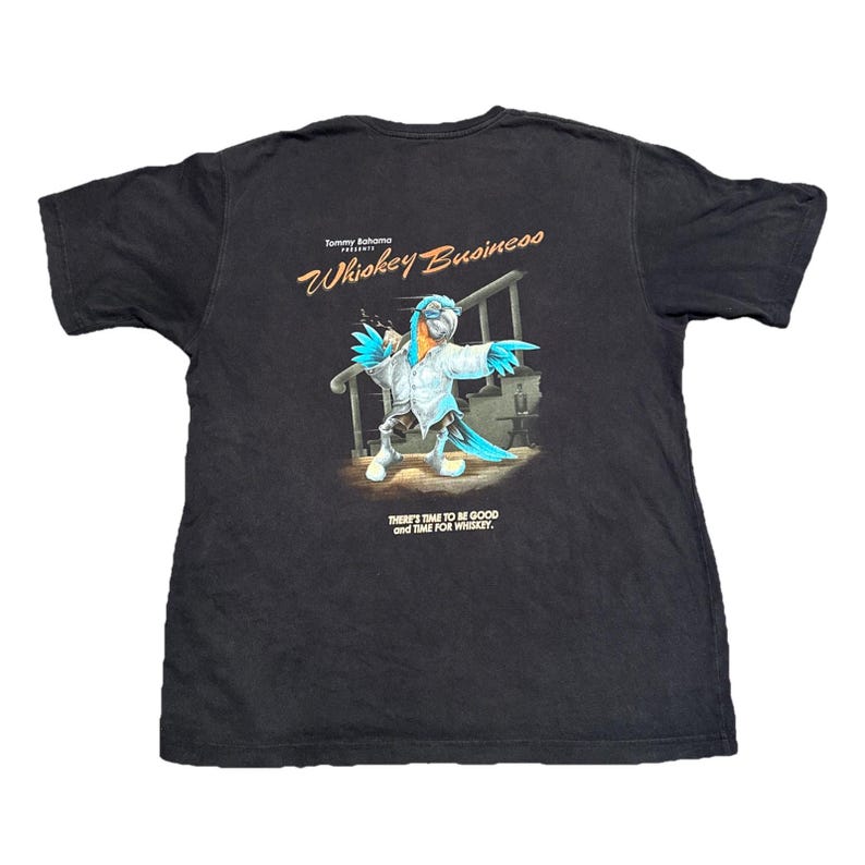 May include: Black t-shirt featuring a colorful parrot illustration with the text "Whiskey Business" and "There's time to be good and time for whiskey." The parrot is wearing a white shirt and pointing.