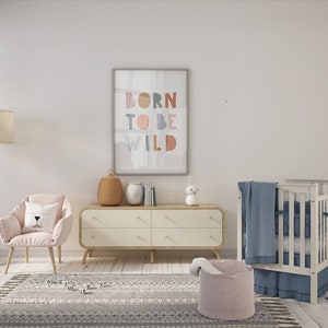 May include: A white crib with a blue blanket and a pink and white storage basket. A white dresser with four drawers sits next to the crib. A pink armchair with a white pillow sits in front of the dresser. A framed print with the text "Born to be Wild" hangs on the wall.
