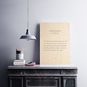 May include: A beige wood print featuring a quote from Charles Dickens's "A Christmas Carol": "I will honour Christmas in my heart, and try to keep it all the year. I will live in the Past, the Present, and the Future. The Spirits of all Three shall strive within me. I will not shut out the lessons that they teach."