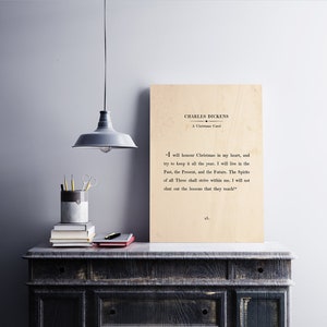 May include: A beige wood print featuring a quote from Charles Dickens's "A Christmas Carol": "I will honour Christmas in my heart, and try to keep it all the year. I will live in the Past, the Present, and the Future. The Spirits of all Three shall strive within me. I will not shut out the lessons that they teach."