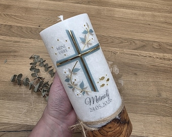 Könnte beinhalten: Eine weiße zylindrische Kerze mit einem gold-blauen Kreuz, floralen Akzenten und drei kleinen goldenen Fischen. Der Text lautet MEINE TAUFE, Meinolf und 24.05.2026. Der Fuß ist mit einer natürlichen Holzscheibe und einer Juteschnur umwickelt.