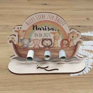 Könnte beinhalten: Holzspardose in Form der Arche Noah, mit Regenbogen und Zeichentricktieren. Der Text "ALLES LIEBE ZUR TAUFE" und der Name "Marisa" mit dem Datum "04.04.2025" sind sichtbar. Sie hat Schlitze zum Einwerfen von gerollten Geldscheinen.