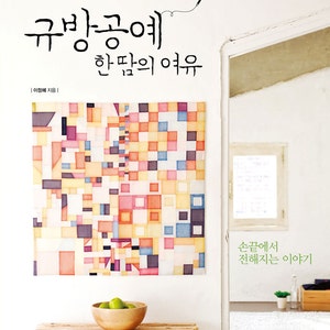 Op de afbeelding: Een boekomslag met een witte achtergrond en een kleurrijk geometrisch ontwerp. De titel is "규방공예" (Gyu-bang Gong-ye) in het Koreaans, wat zich vertaalt naar "Traditioneel Koreaans handwerk". De ondertitel is "한땀의 여유" (Han-ttam-ui Yeo-yu), wat zich vertaalt naar "De rust van één steek". De tekst "손끝에서 전해지는 이야기" (Son-kkeut-eseo Jeon-hae-jineun I-yagi) staat ook op de omslag, wat zich vertaalt naar "Het verhaal dat door de vingertoppen wordt verteld".