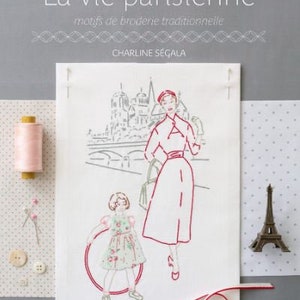 May include: A book cover with the title "La vie parisienne" in a decorative font. The subtitle is "motifs de broderie traditionnelle" and the author is "CHARLINE SEGALA". The cover features a black and white illustration of a woman and a girl in Paris.