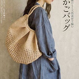 Könnte beinhalten: Eine beige gehäkelte Tasche mit runder Form und offenem Webmuster. Die Tasche hat zwei Henkel und wird über der Schulter getragen. Das Bild enthält auch japanischen Text.
