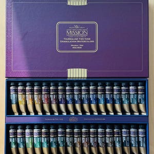 Op de afbeelding: Een set van 34 waterverfverf in tubes, met het label "Tourmaline Two Tone Granulation Watercolors" van Mission Gold Class Watercolors. De tubes zijn gerangschikt in twee rijen van 17, met een blauwe achtergrond.
