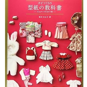 May include: A red book titled "Obitsu 11 no Katagami no Kyokasho" with various doll clothes and accessories arranged on a red surface. The clothes include skirts, dresses, jackets, and a bunny costume.