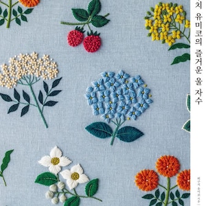 Könnte beinhalten: Nahaufnahme eines hellblauen Stoffes mit verschiedenen gestickten Blumen in verschiedenen Farben, darunter Orange, Gelb, Weiß, Rot, Blau und Grün. Der Text "하루치 야무진 꽃들을 위한 자수" ist in Koreanisch auf der rechten Seite des Bildes geschrieben.