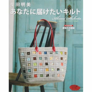May include: A light grey tote bag with a patchwork design, featuring a woven pattern of colourful squares. The bag has red handles and is displayed in front of a book with Japanese text. The book's title is "あなたに届けたいキルト" by Akemi Shibata.