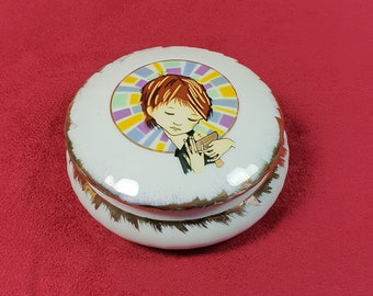 May include: White ceramic trinket box with a gold rim and a colorful image of a young person holding a bird.