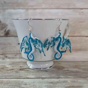 May include: A pair of dangle earrings featuring a blue and white embroidered dragon design.