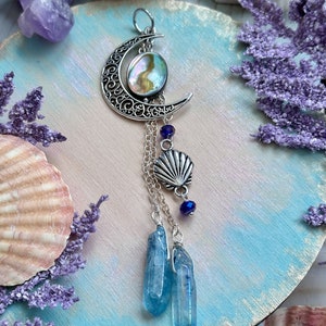May include: A silver crescent moon charm with a iridescent abalone shell pendant, dangling chains with a silver seashell charm and blue crystal points.